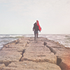 photo: a person standing at the edge of a stone bridge, looking out at the sea